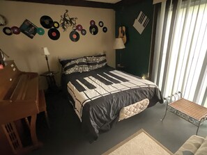Ein Schlafzimmer mit Bett, Schreibtisch, Lampe und einem Fenster mit Jalousien.