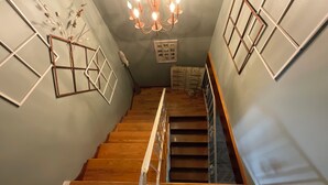 En trappe med trætrin og gelænder i metal, der fører op til en platform med en lysekrone og indrammede billeder.