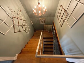 Eine Treppe mit Holzboden und Metallgeländer, die zu einer Zwischenebene mit einem Kronleuchter und gerahmten Bildern führt.