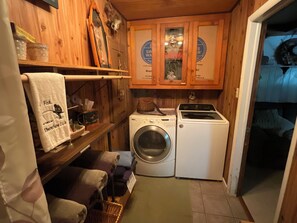 A compact laundry room with a washing machine and dryer, wooden cabinets, and a towel rack with a humorous towel. - Unique 3+bedroom house at the beautiful Lake of Egypt (Marion)