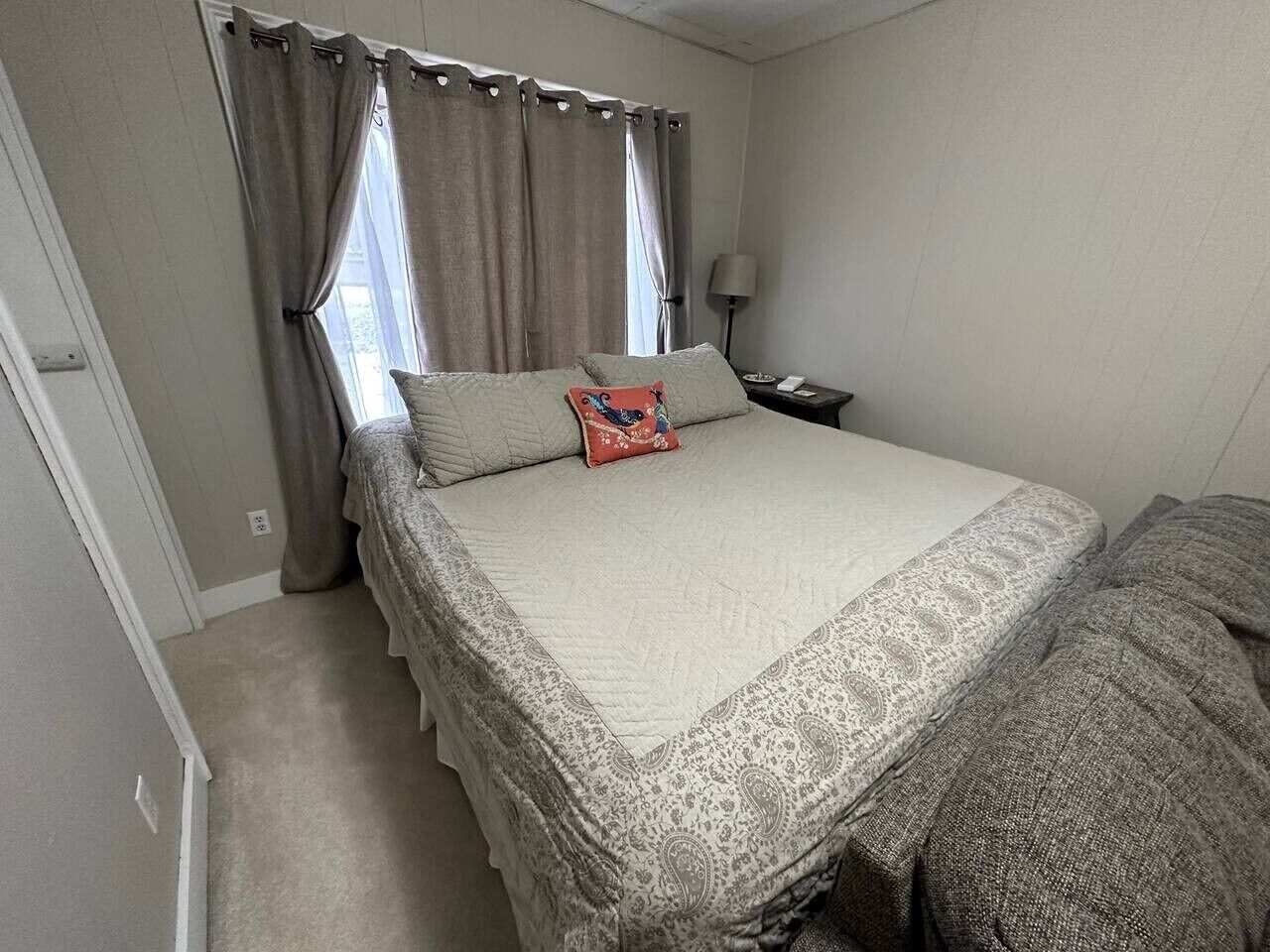 A bedroom with a bed, curtains, a nightstand, and a lamp.