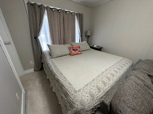 A bedroom with a bed, curtains, a nightstand, and a lamp.