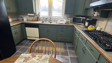 Une cuisine avec des meubles de couleur verte, une cuisinière, un four à micro-ondes et une fenêtre avec un rideau.