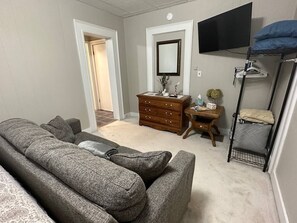 A room with a grey sofa, a wooden dresser, a television mounted on the wall, and a bunk bed with a blue pillow.