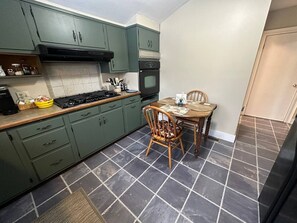 A kitchen with green cabinets, a stove, and a dining table with chairs.