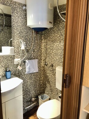 A bathroom with a mosaic tile wall, a white toilet, a sink with a blue soap dispenser, and a white towel hanging on a rack. - Vrbo Property (Verona)