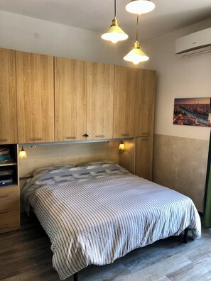 A bedroom with a bed, wooden wardrobe, pendant lights, and a cityscape painting. - Vrbo Property (Verona)
