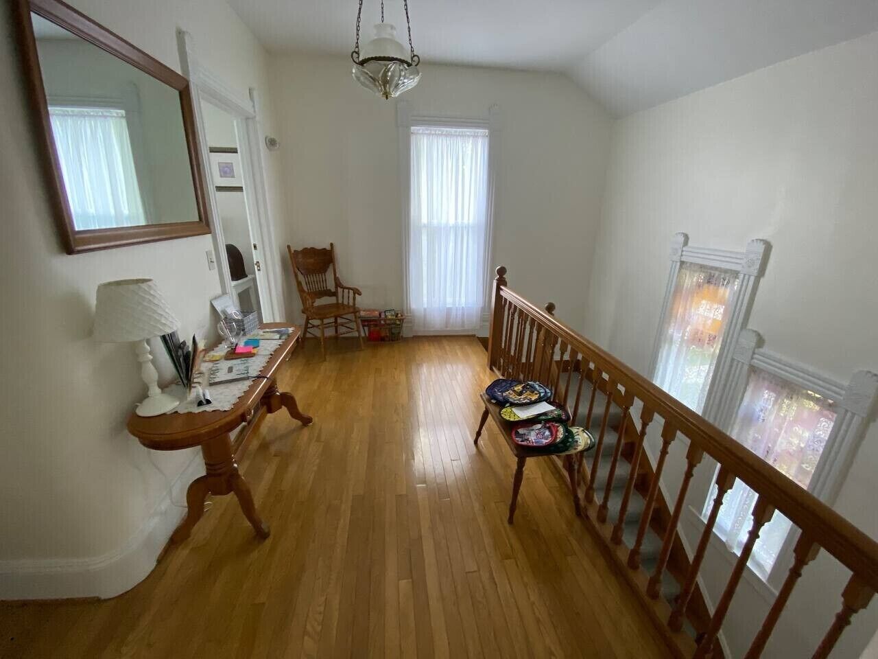 A room with a wooden floor, a dining table with chairs, a mirror, and a staircase with a railing.