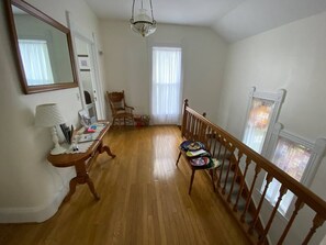A room with a wooden floor, a dining table with chairs, a mirror, and a staircase with a railing.