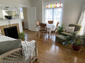 A living room with a fireplace, a dining table with chairs, a sofa, and a window with a view.