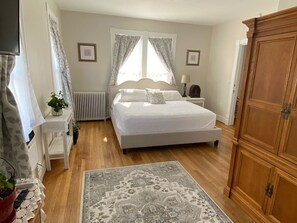 A bedroom with a bed, bedside table, lamp, radiator, and wooden wardrobe.