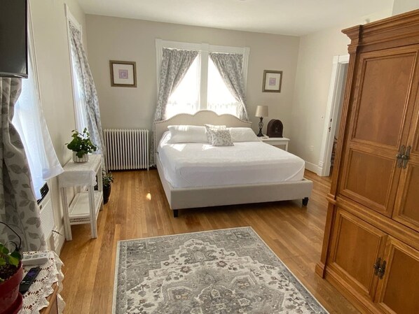 A bedroom with a bed, bedside table, lamp, radiator, and wooden wardrobe.