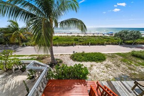 A beach view from a wooden deck with a railing, palm trees, and a clear sky. - Miami Beachfront Oasis with Stunning Ocean Views (Miami Beach)