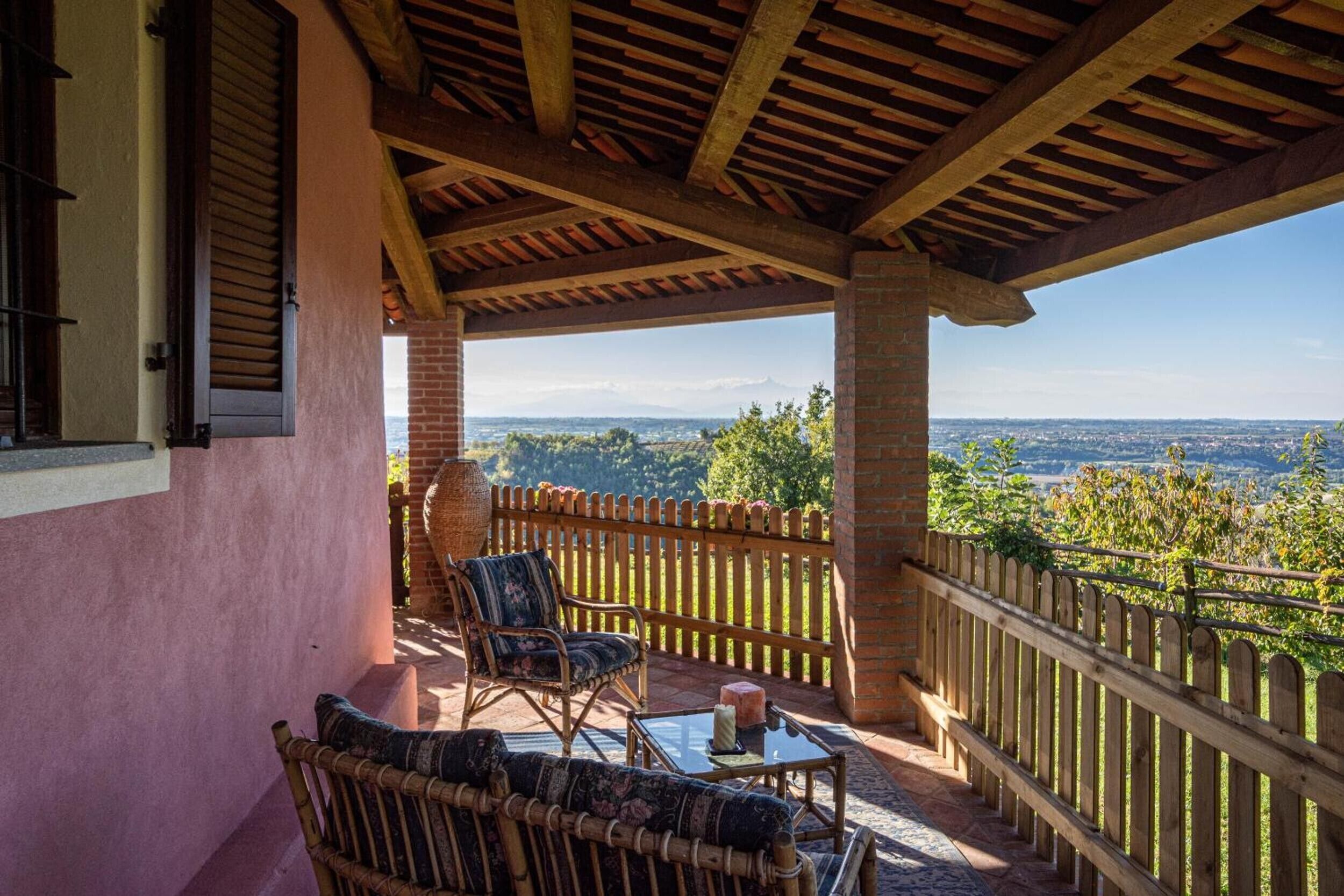 A covered outdoor seating area with wicker furniture and a glass table, overlooking a scenic landscape.