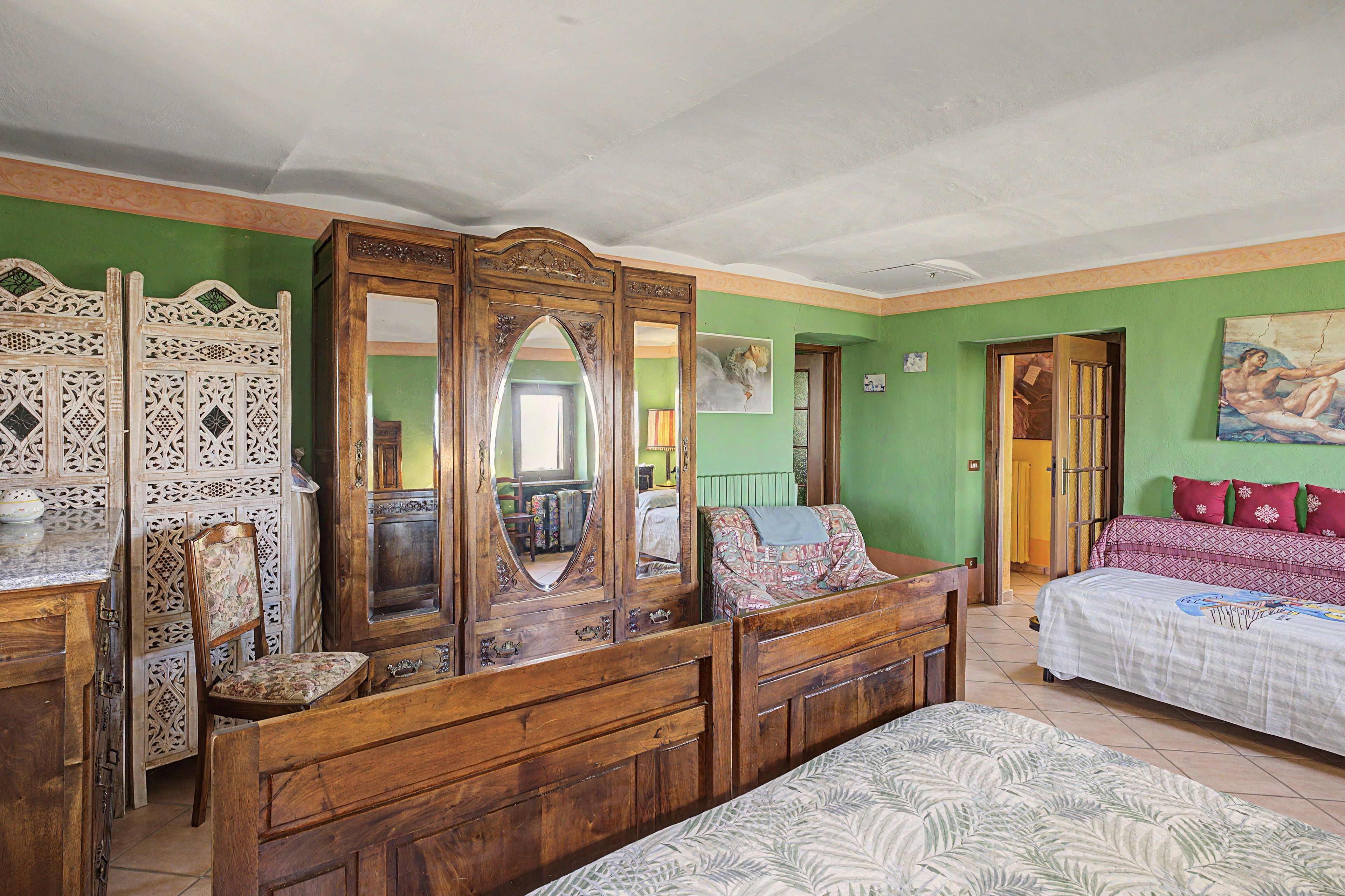 Una stanza con un'ampia armatura in legno, un letto con biancheria a motivi e una parete verde.