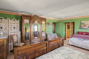 A room with a large wooden wardrobe, a bed with patterned bedding, and a green wall.