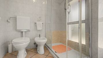 A bathroom with a toilet, bidet, and a glass-enclosed shower area.