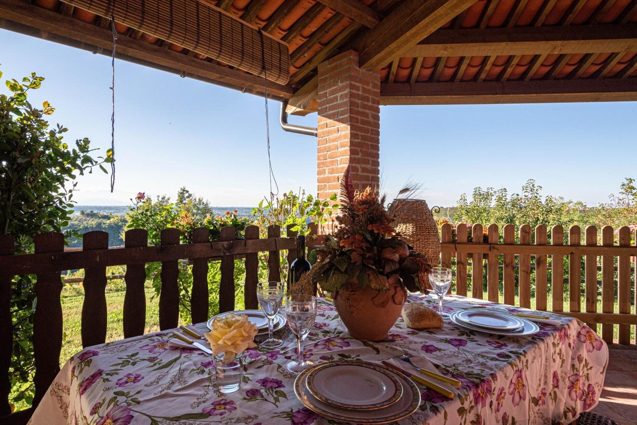An outdoor dining area with a table set for two, a brick chimney, and a view of the countryside.