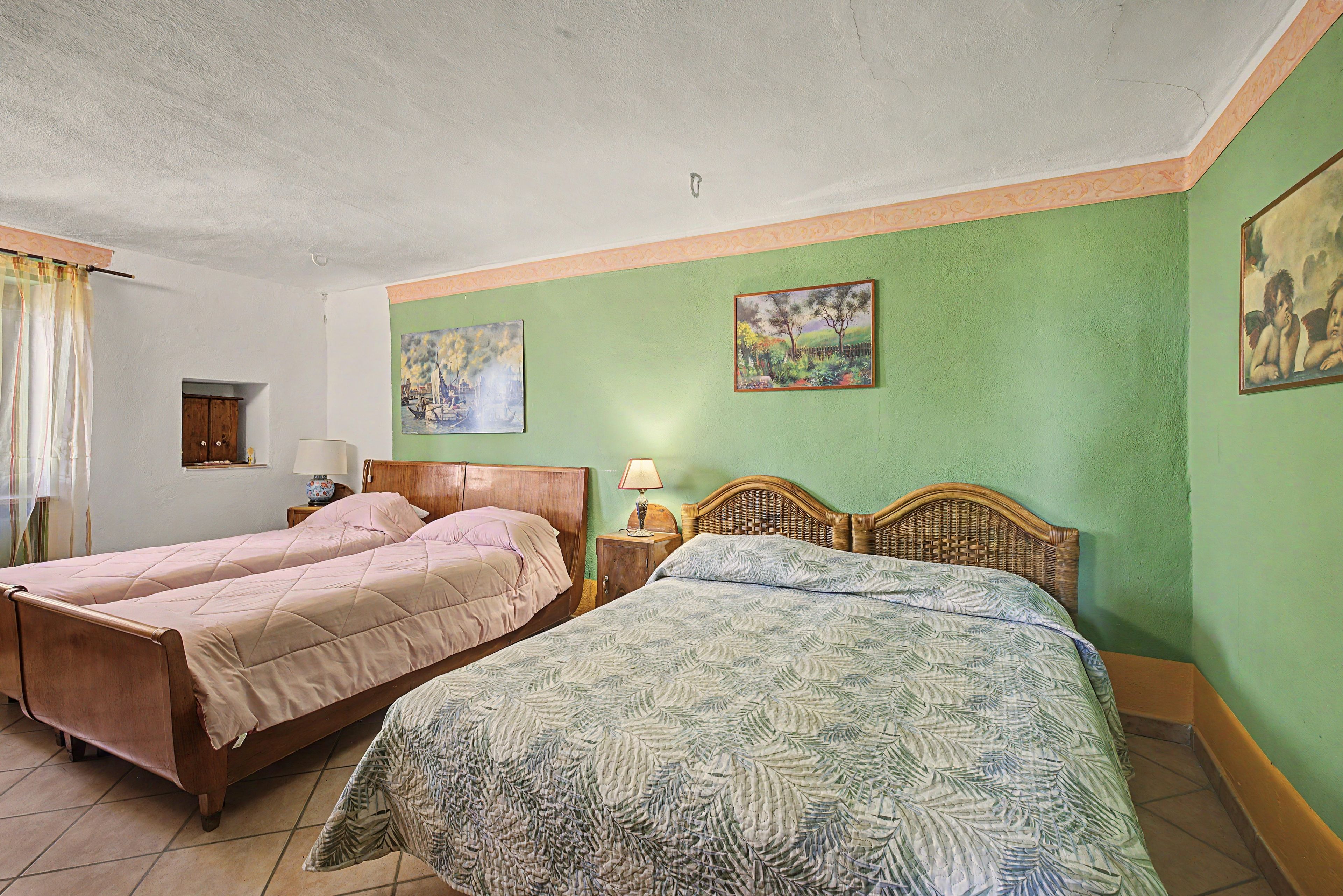 A room with two beds, a small window, and two paintings on the wall.