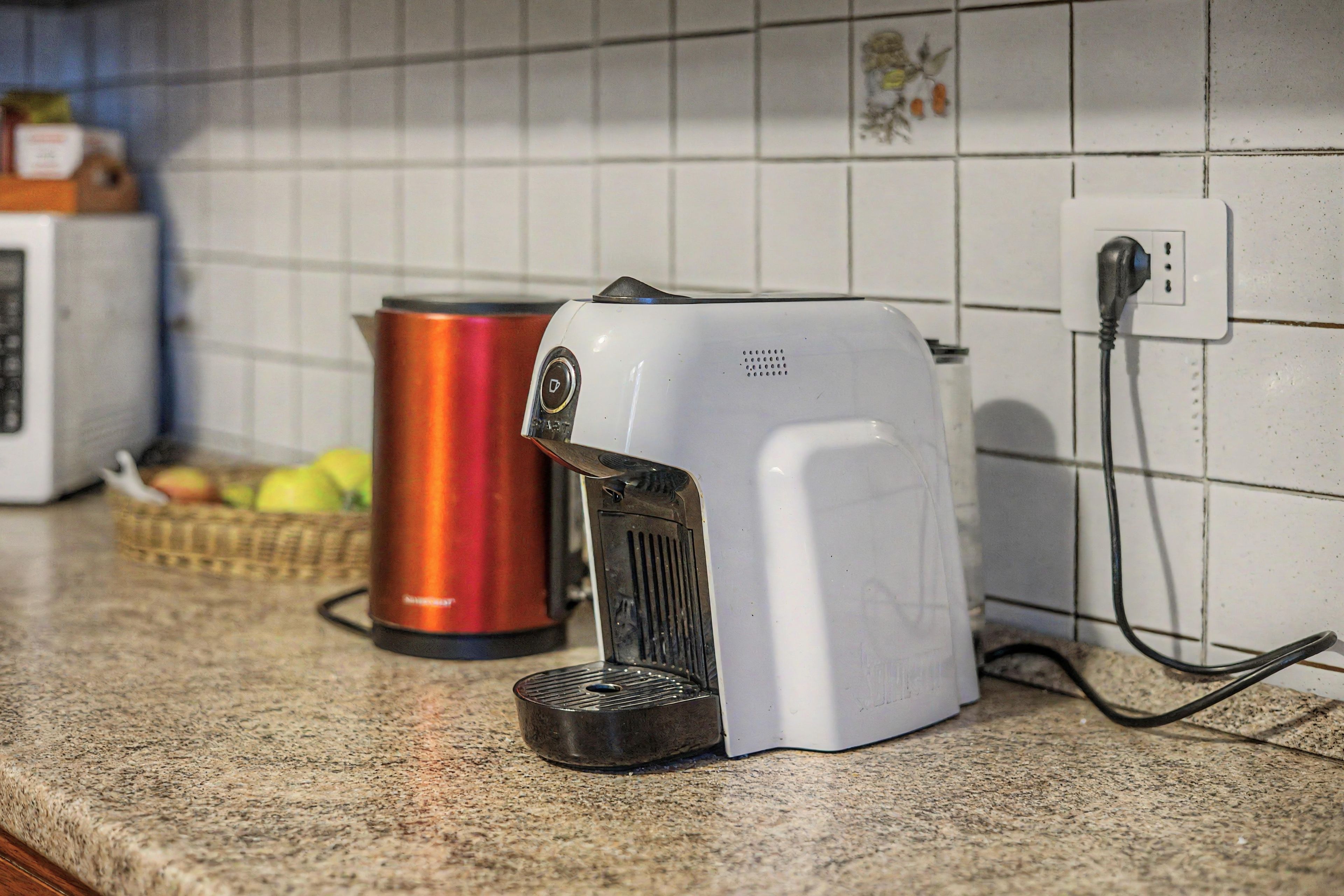 A kitchen with a coffee maker, a red kettle, and a microwave.