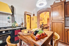 Cocina con estufa, lavamanos y mesa de comedor servida con verduras y una botella.
