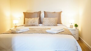 A neatly made double bed with two pillows, a bedside table with a lamp, and a small plant on the nightstand. - Cozy One-Bedroom Retreat with Private Patio & Sunrise Views in Madeira (Ponta do Sol)