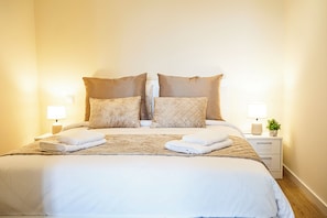 A neatly made double bed with two pillows, a bedside table with a lamp, and a small plant on the nightstand. - Cozy One-Bedroom Retreat with Private Patio & Sunrise Views in Madeira (Ponta do Sol)