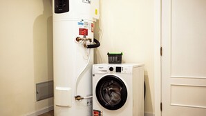A compact washer and dryer unit in a room with a white door and wooden flooring. - Cozy One-Bedroom Retreat with Private Patio & Sunrise Views in Madeira (Ponta do Sol)