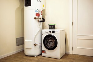 A compact washer and dryer unit in a room with a white door and wooden flooring. - Cozy One-Bedroom Retreat with Private Patio & Sunrise Views in Madeira (Ponta do Sol)