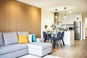 A modern living room with a grey sectional sofa, a dining table with chairs, and a kitchen area with a refrigerator and pendant lights. - Cozy One-Bedroom Retreat with Private Patio & Sunrise Views in Madeira (Ponta do Sol)