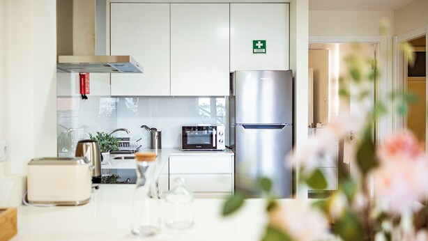 A modern kitchen with white cabinets, a stainless steel refrigerator, a microwave, and a toaster. - Cozy One-Bedroom Retreat with Private Patio & Sunrise Views in Madeira (Ponta do Sol)
