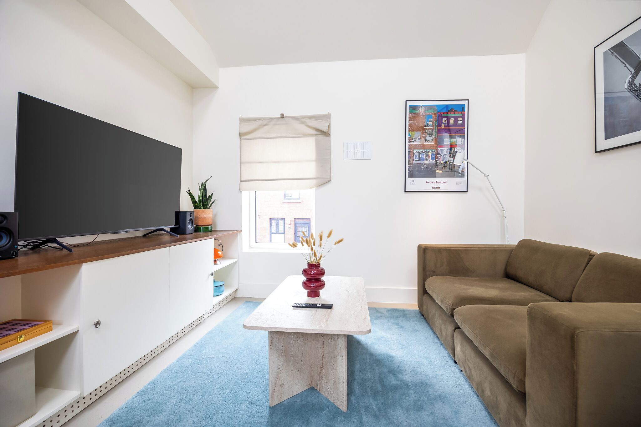 A living room with a flat-screen TV, a brown sofa, a coffee table with a vase, and a framed picture on the wall.