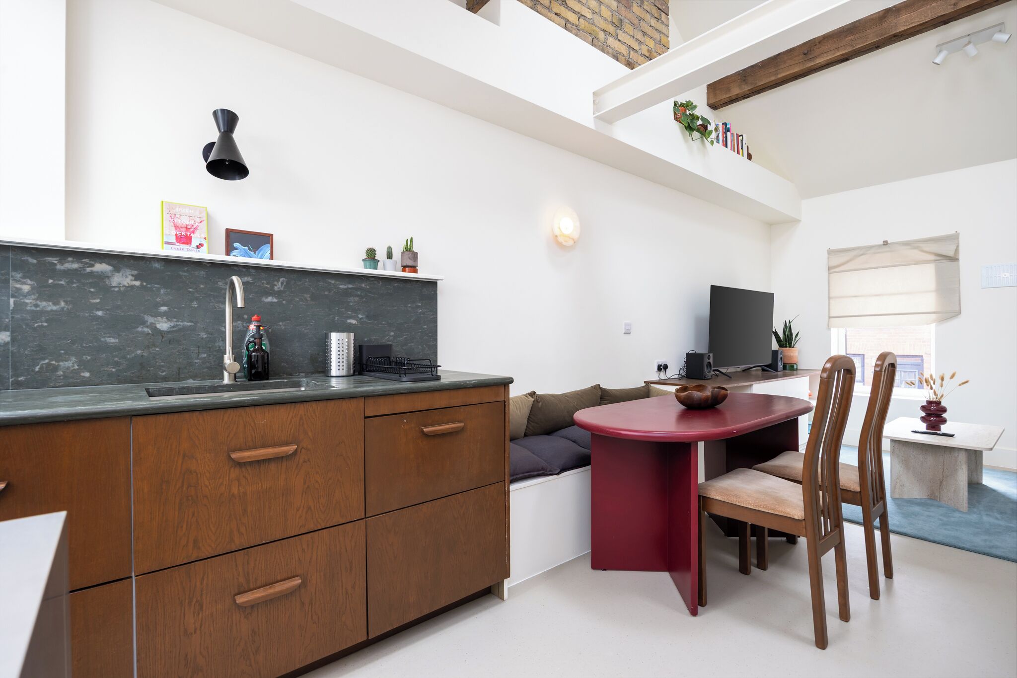 A modern kitchen with a built-in stove, a dining area with a red table and wooden chairs, and a television on a stand.