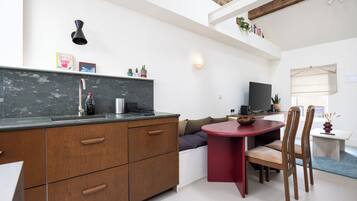 A modern kitchen with a built-in stove, a dining area with a red table and wooden chairs, and a television on a stand.
