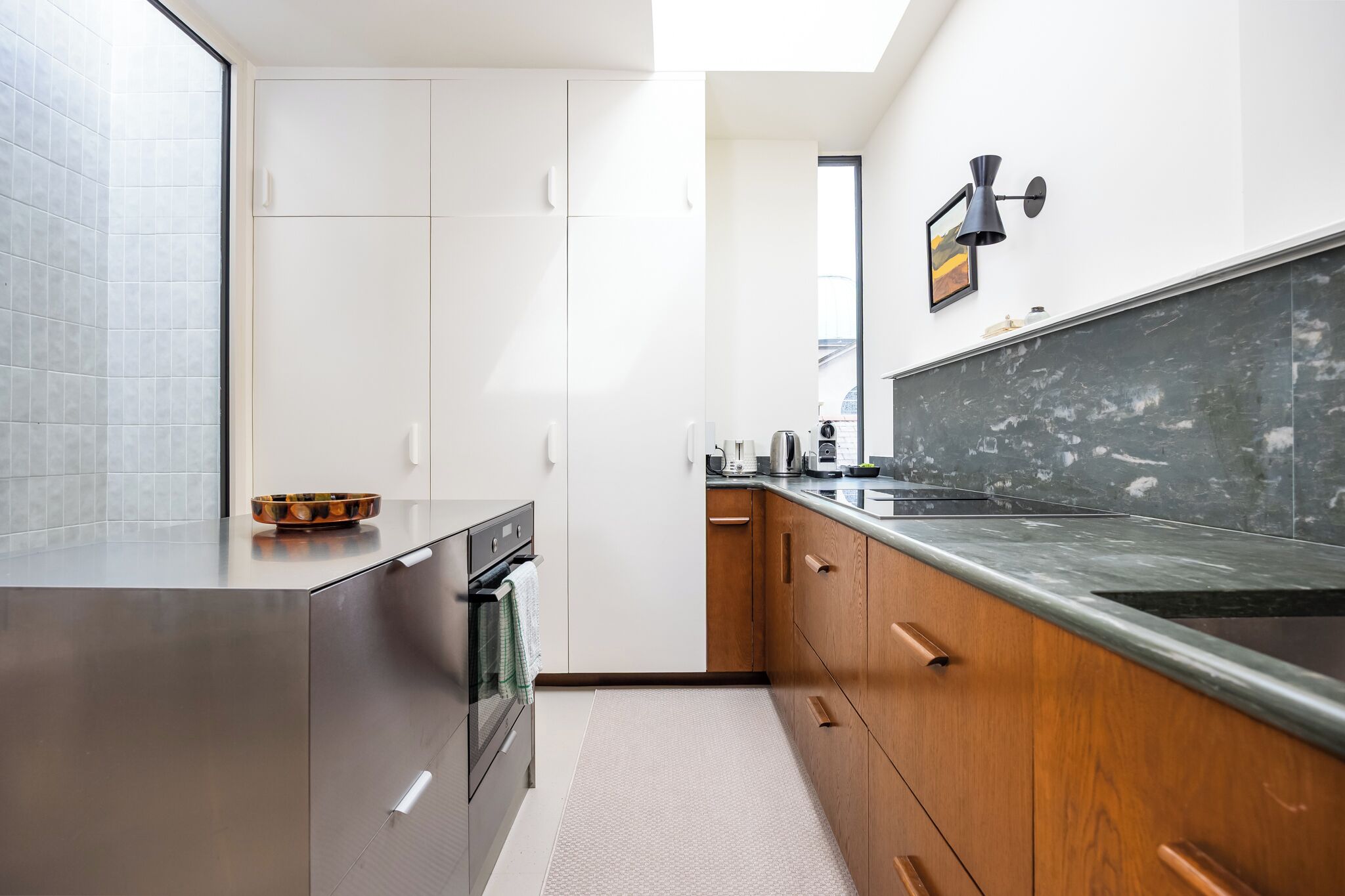 A modern kitchen with a stainless steel oven, wooden cabinets, a marble countertop, and a black pendant light.