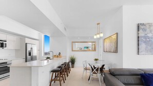 Una cocina moderna con una isla central, un área de comedor con una mesa y sillas blancas y un sofá gris.