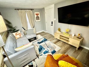 A living room with a sofa, a coffee table, a TV, a wooden cabinet, and a door. - Private Midtown Atl Apartment -  5 minutes from Mercedes Benz Stadium (Atlanta)