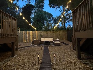 Un espace extérieur aménagé avec une terrasse en bois, un canapé central et des guirlandes lumineuses.