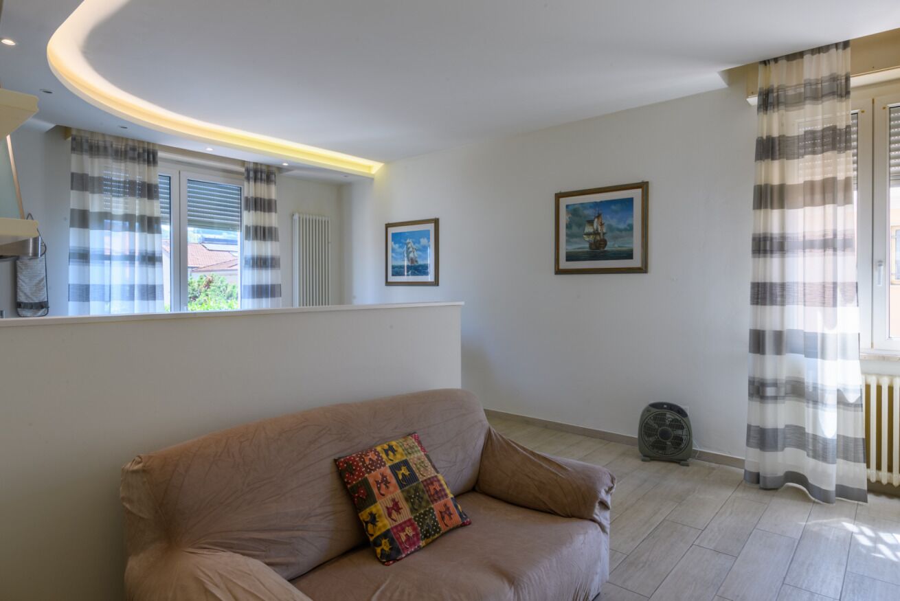 A living room with a sofa, a cushion, a radiator, a fan, and two framed pictures on the wall.