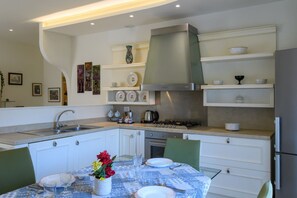 A modern kitchen with white cabinetry, a gas stove, and a stainless steel range hood. There is a dining table set with plates and glasses. - GuestHost - Flaminia 36 Apartment (Pesaro)