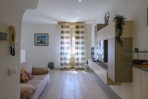 A modern living room with a sofa, a television, and a glass shelf. - GuestHost - Flaminia 36 Apartment (Pesaro)
