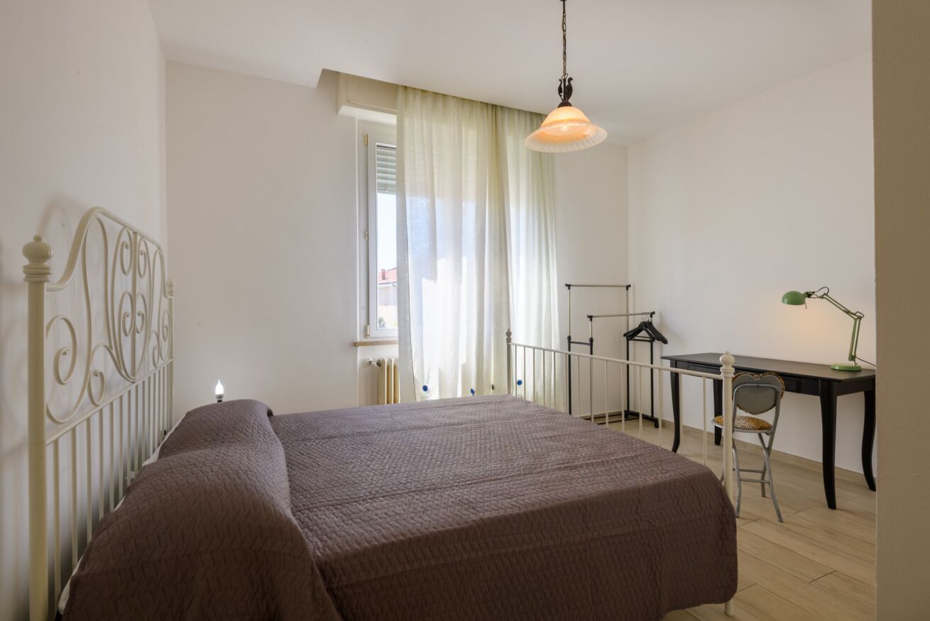 A bedroom with a bed, a desk, a chair, and a hanging light fixture.