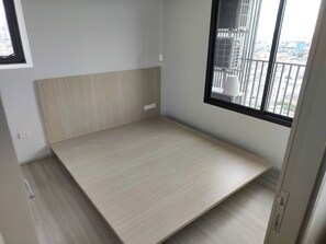 Ein Zimmer mit Holzboden, weißer Wand und Fenster mit Blick auf Gebäude.