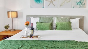Une chambre d’hôtel bien rangée, avec un lit, une table de chevet dotée d’une lampe, un plateau avec une bouteille et des verres, et des œuvres d’art accrochées au mur.