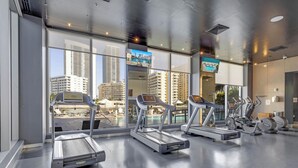 Une salle de sport équipée de tapis de course, de vélos d’appartement et offrant une vue sur la piscine.