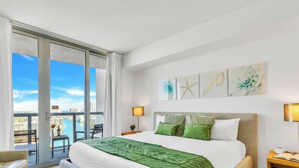 Une chambre d’hôtel avec un grand lit, un balcon donnant sur la ville et des œuvres d’art accrochées au mur.