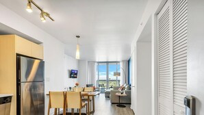 Une cuisine moderne dotée d’un réfrigérateur encastré, un coin repas avec des chaises et une table, et un espace de vie avec un canapé et un téléviseur.