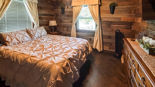 A wooden cabin bedroom with a bed, nightstand, dresser, and two windows with curtains. - *NEW* River Valley Retreat ~ directly on White River (Mountain View)