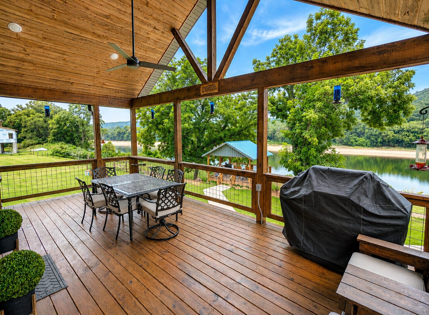 A wooden deck with a table and chairs, overlooking a lake and greenery.