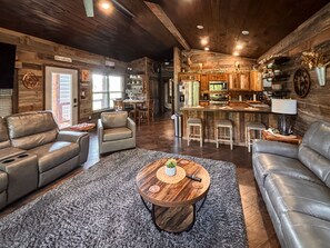 A spacious living room with leather sofas, a wooden coffee table, and a kitchen area with a bar. - *NEW* River Valley Retreat ~ directly on White River (Mountain View)